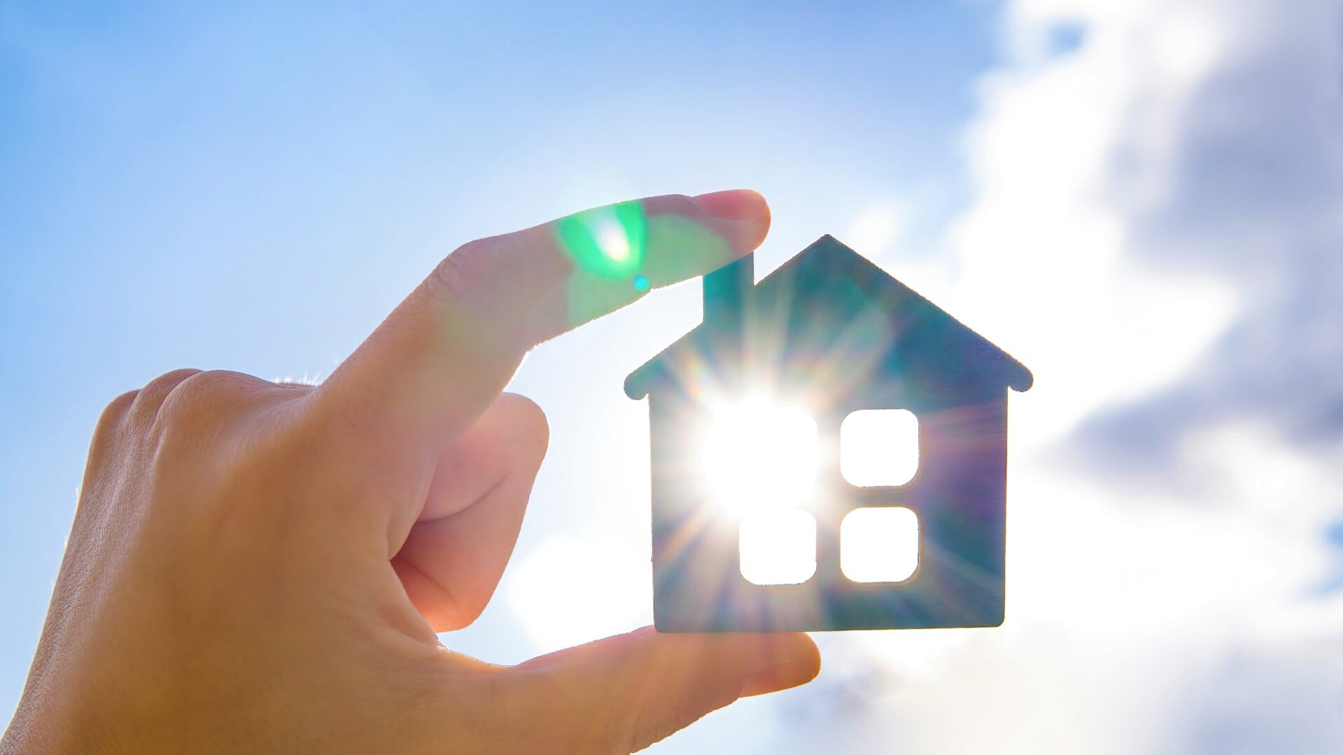 Person hält Miniaturhaus vor die Sonne