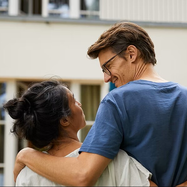 Paar umarmt sich und lächelt vor einem Haus im Freien.