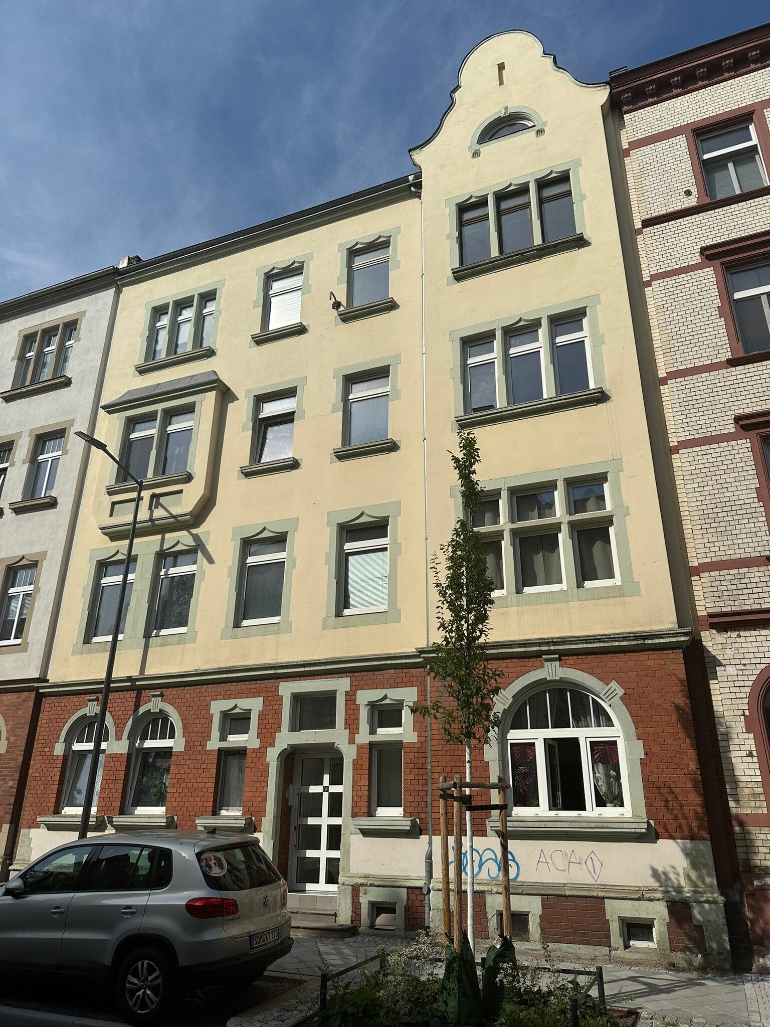 Gelbes Wohnhaus, einzigartige Fenster, Auto davor, blauer Himmel.
