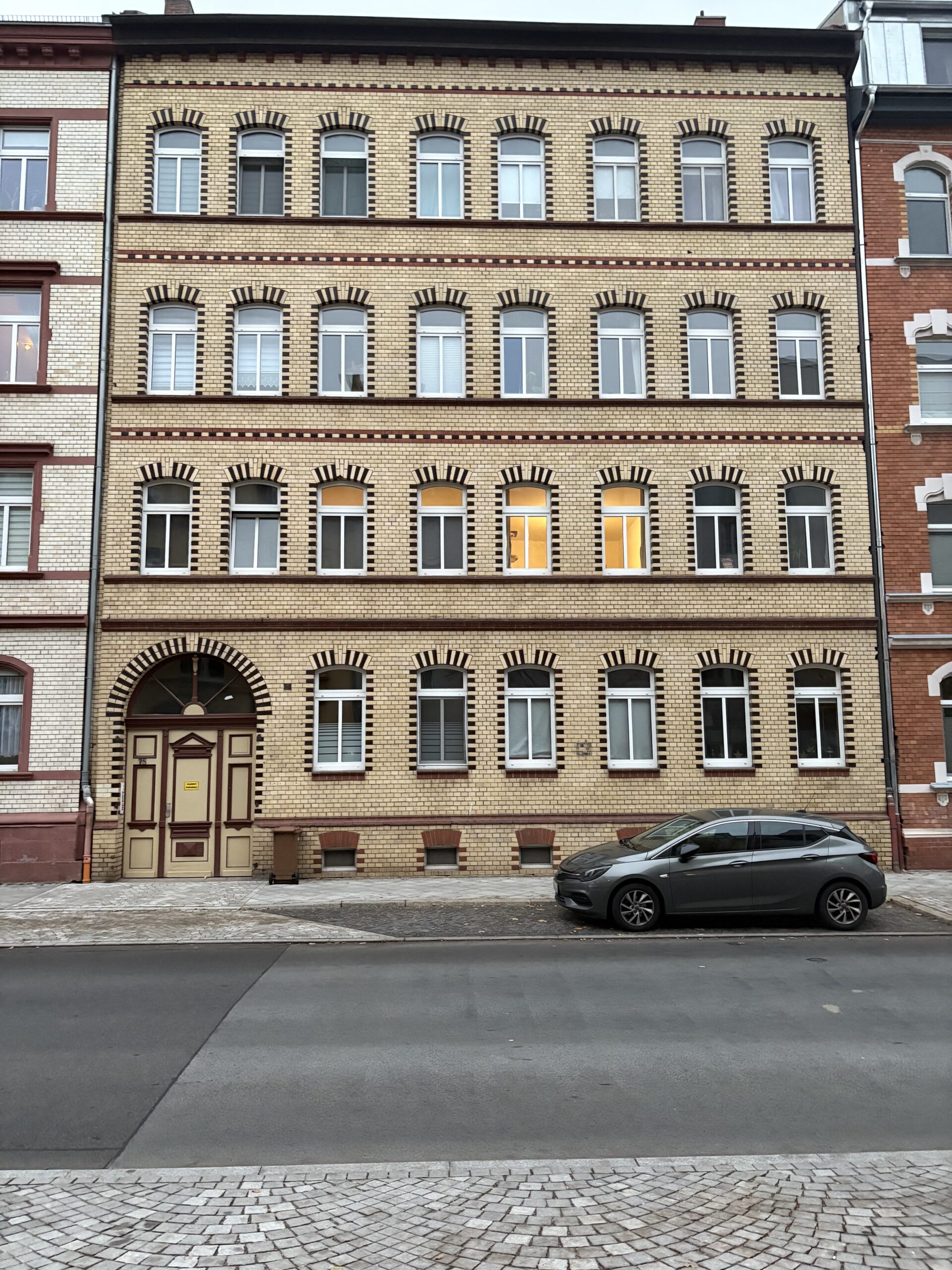 Backsteinbau mit vielen Fenstern, ein Auto davor auf ruhiger Straße.