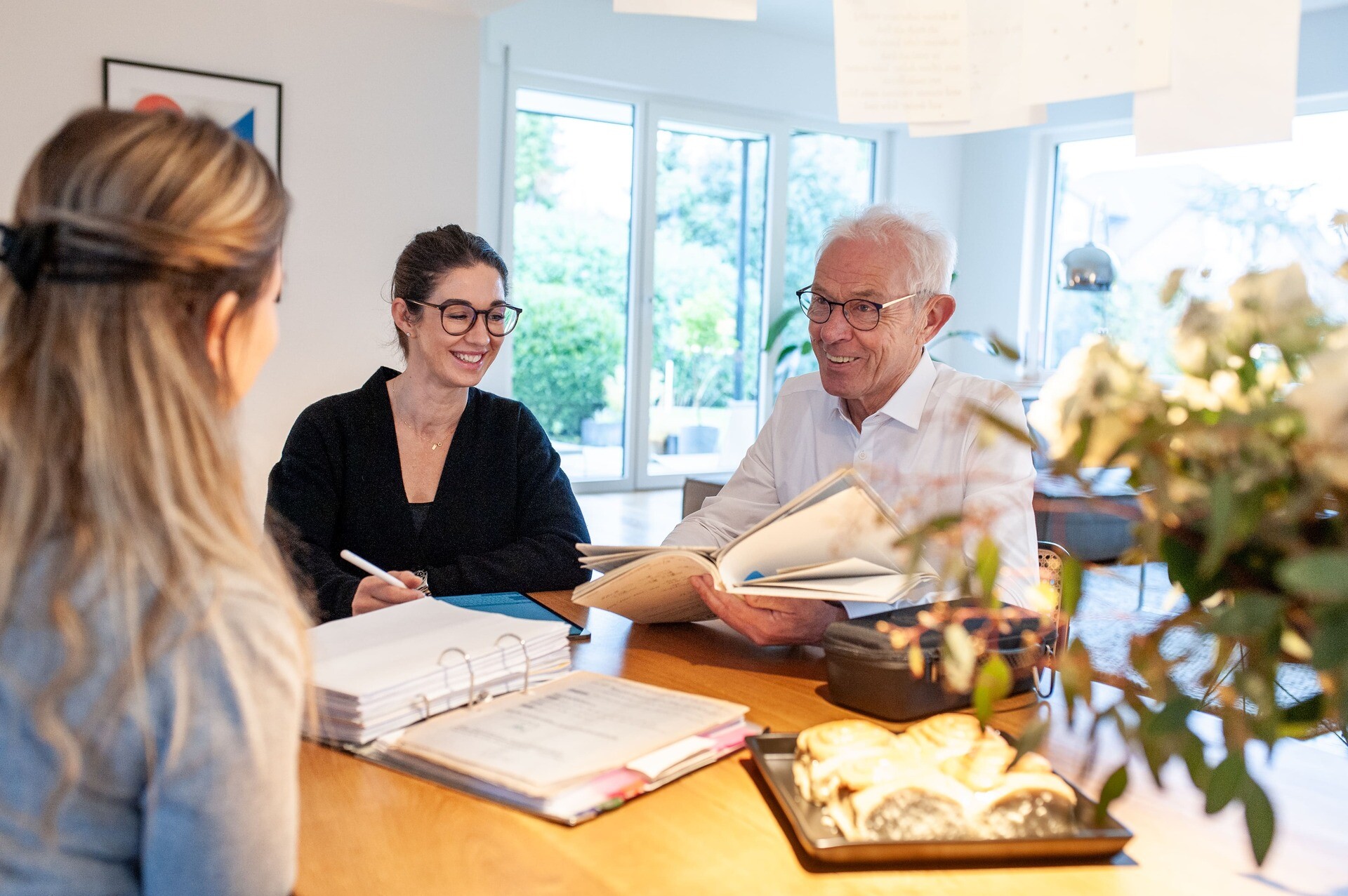 Drei Personen am Tisch besprechen lächelnd Unterlagen.