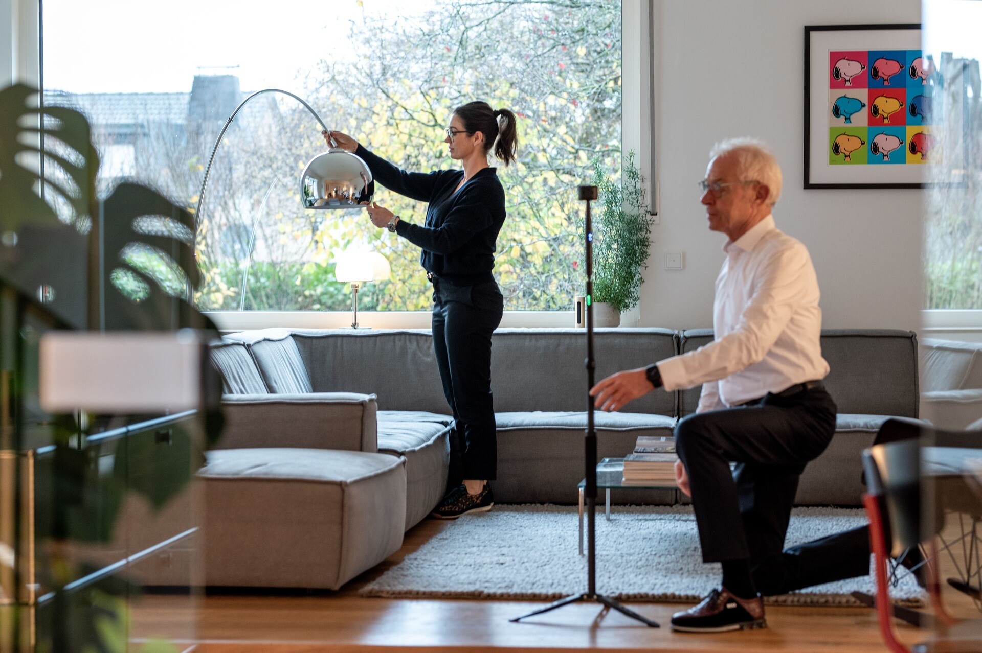 Frau richtet Lampe, Mann kniet im modernen Wohnzimmer.