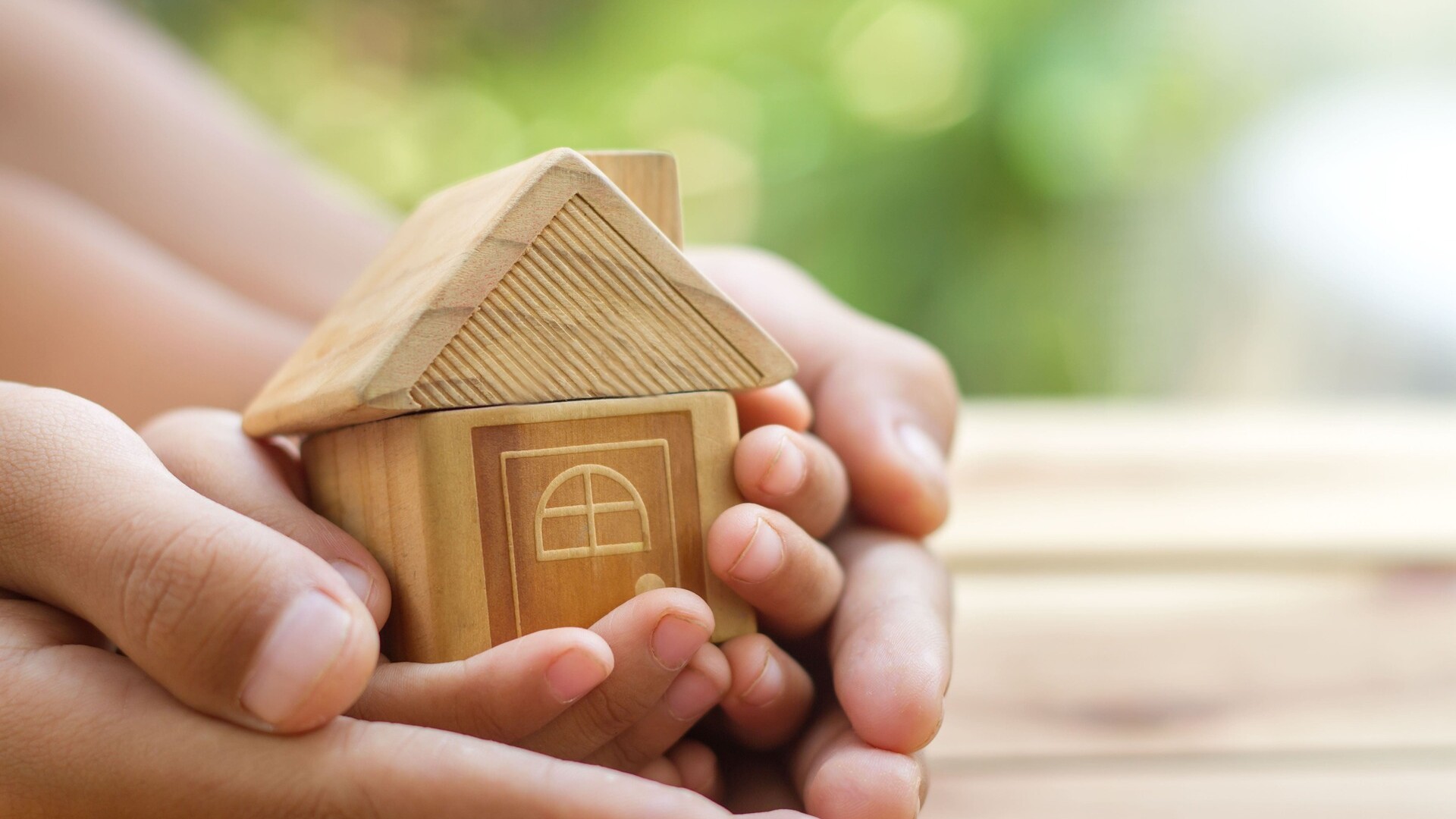Kleine und große Hände halten ein Modellhaus, Symbol für Immobilie geerbt