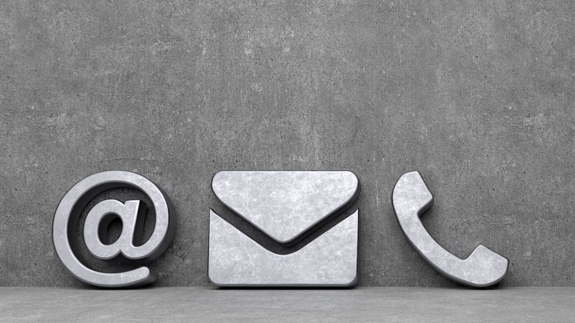Symbole für E-Mail-Kontakt: At-Zeichen, Briefumschlag und Telefonhörer aus Metall vor grauem Hintergrund