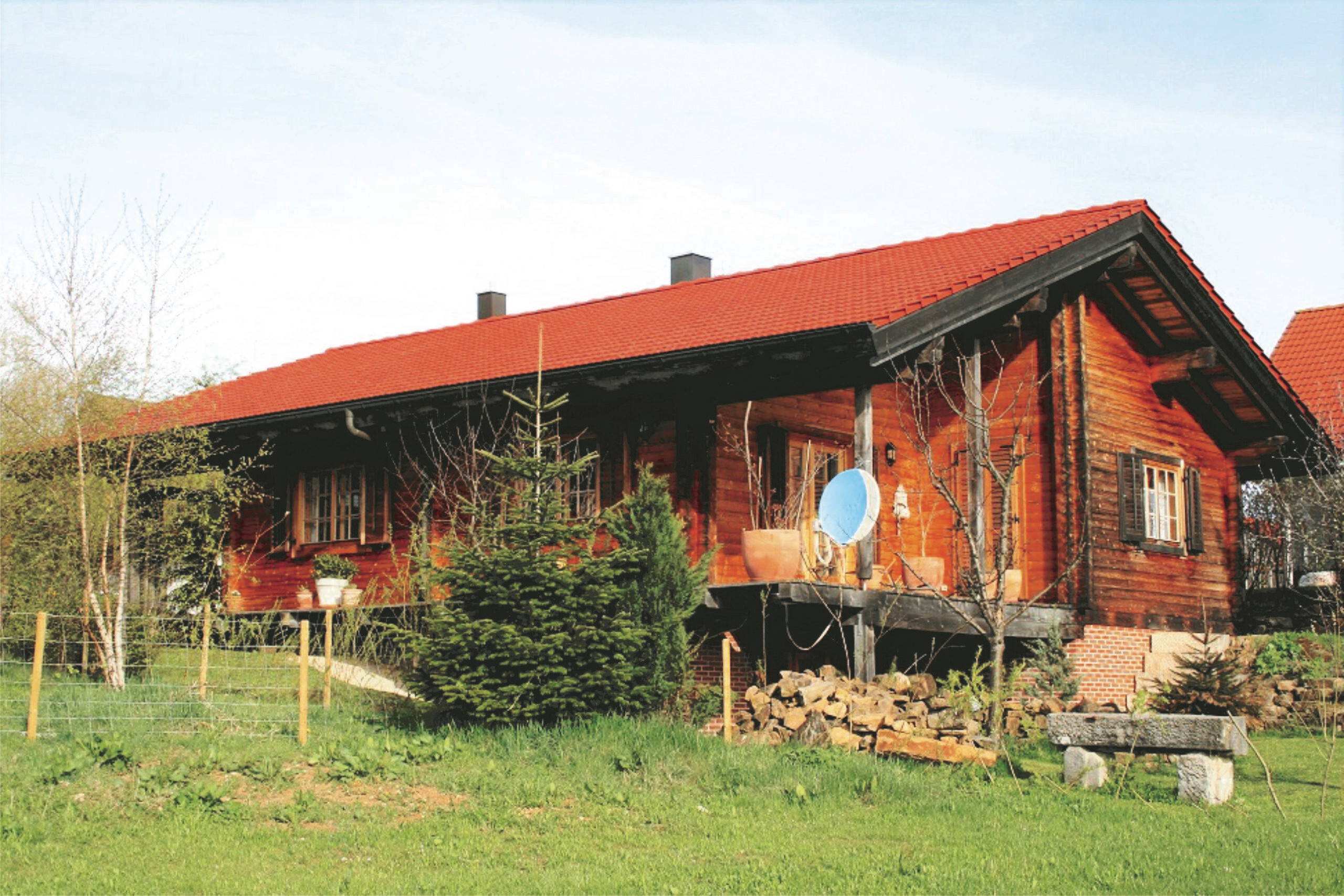 Holzhütte mit rotem Dach, Gras, Bäume und Steinbank
