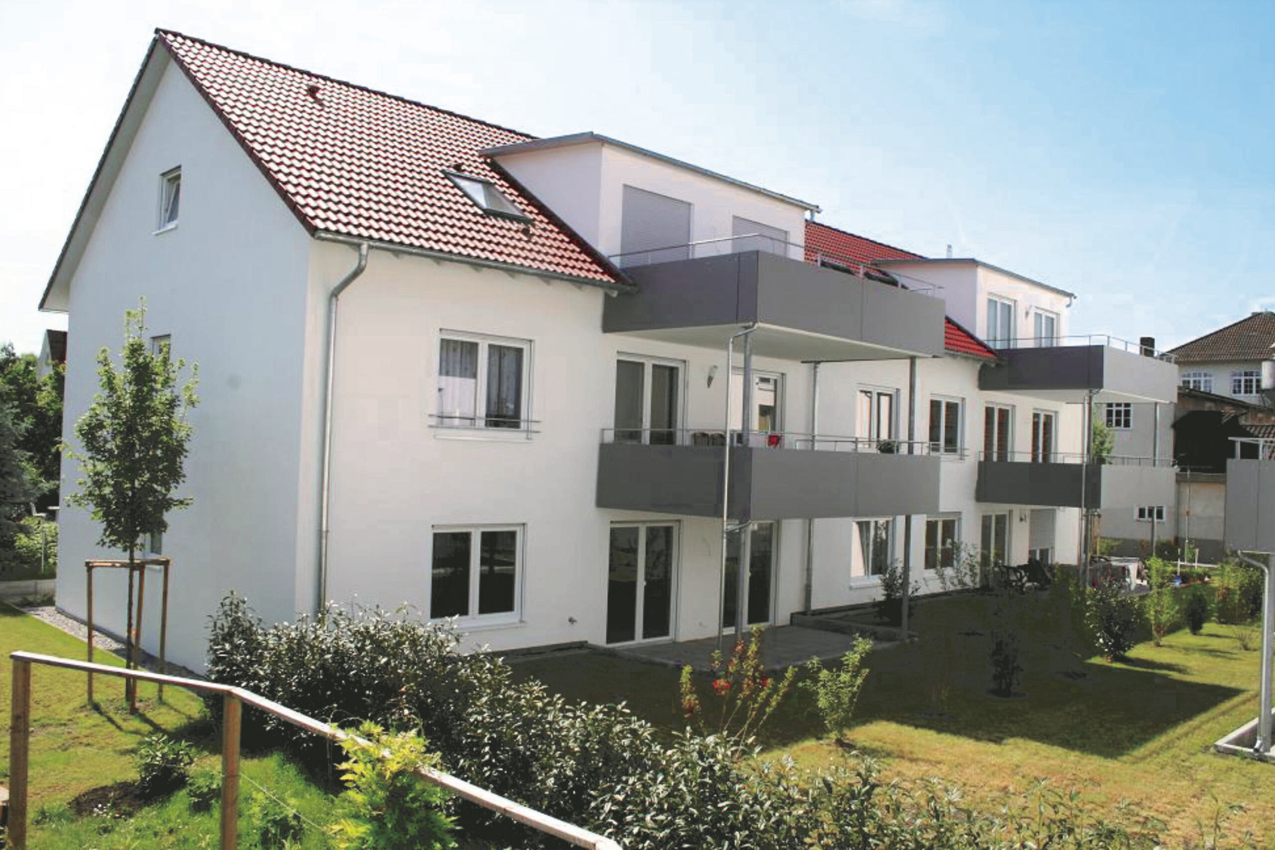 Weiße Wohnung, Balkone, rotes Dach, grüner Garten