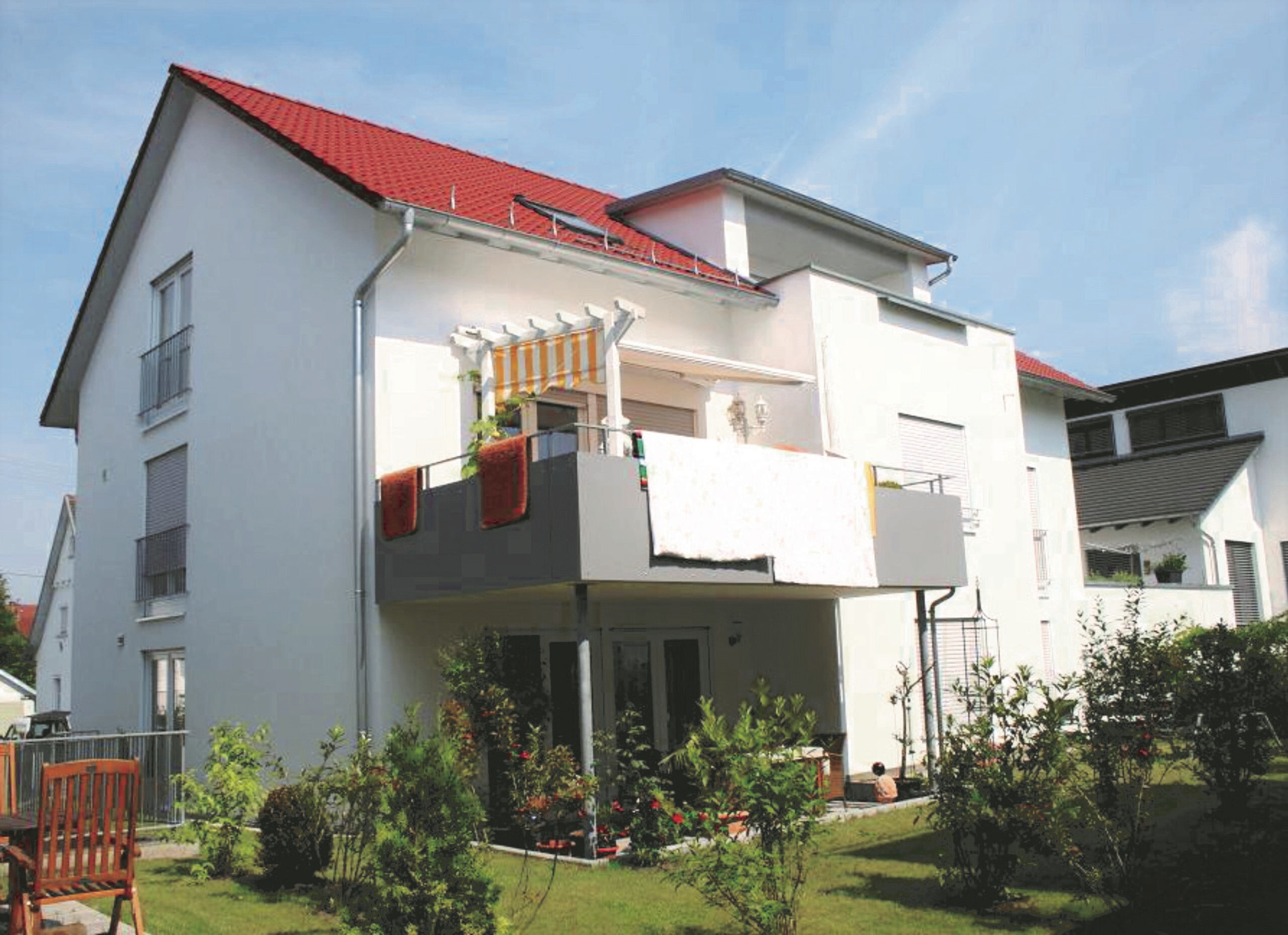 Weißes Haus, rotes Dach, Balkone, grüner Garten