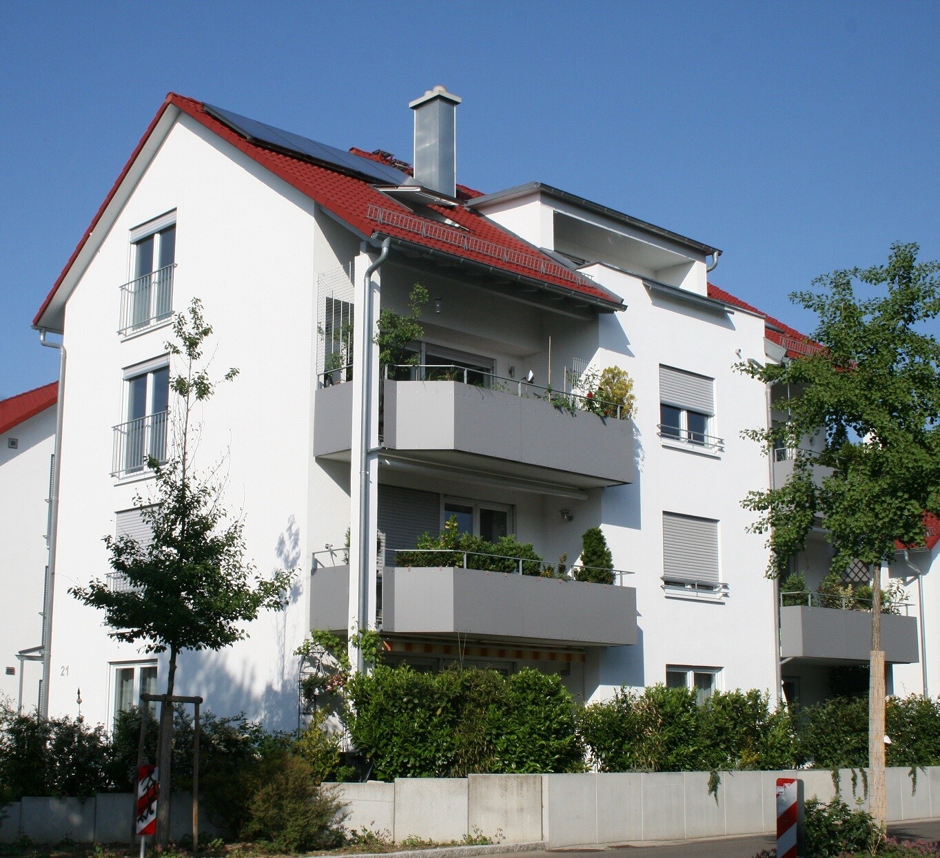 Weiße Wohnung mit Balkonen, rotem Dach und Bäume
