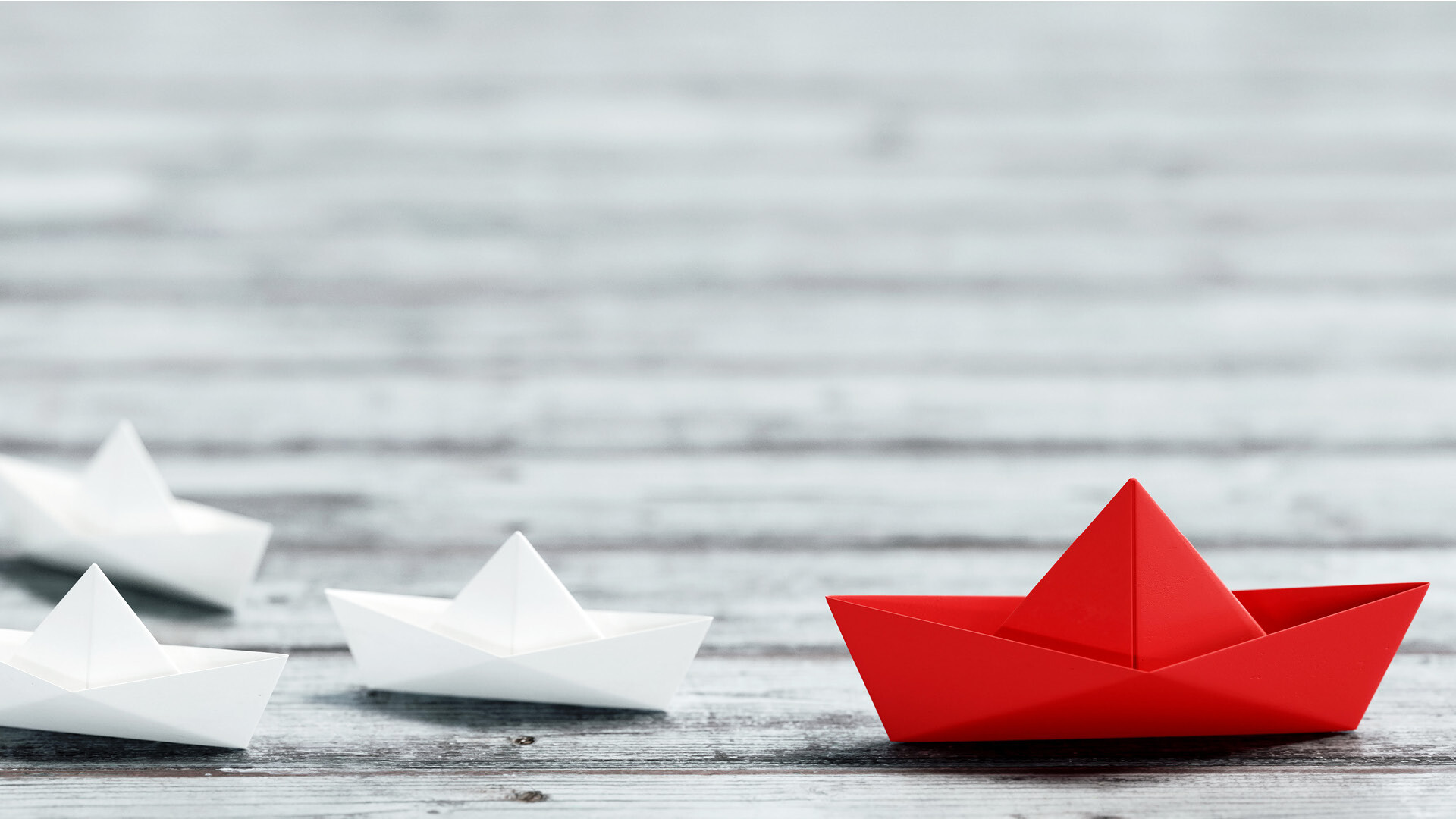 Rotes Boot aus Papier gefaltet neben mehreren weißen Booten