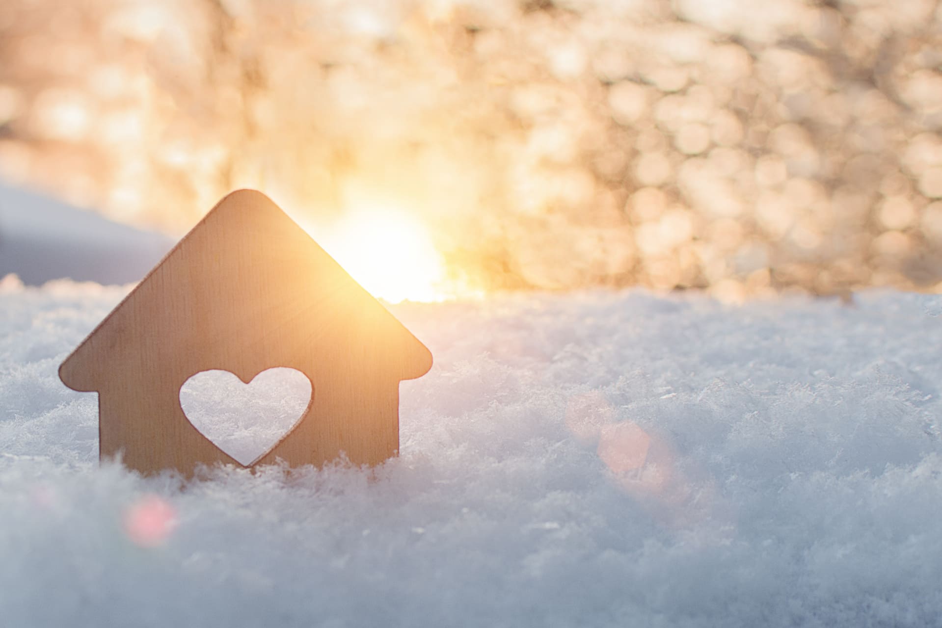 Kleines Holzhaus-Modell mit Herz-Ausschnitt im Schnee bei Sonnenuntergang