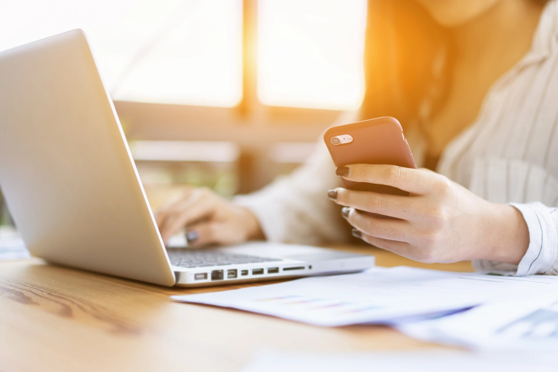 Frau am Schreibtisch mit Laptop, Smartphone und Dokumenten.