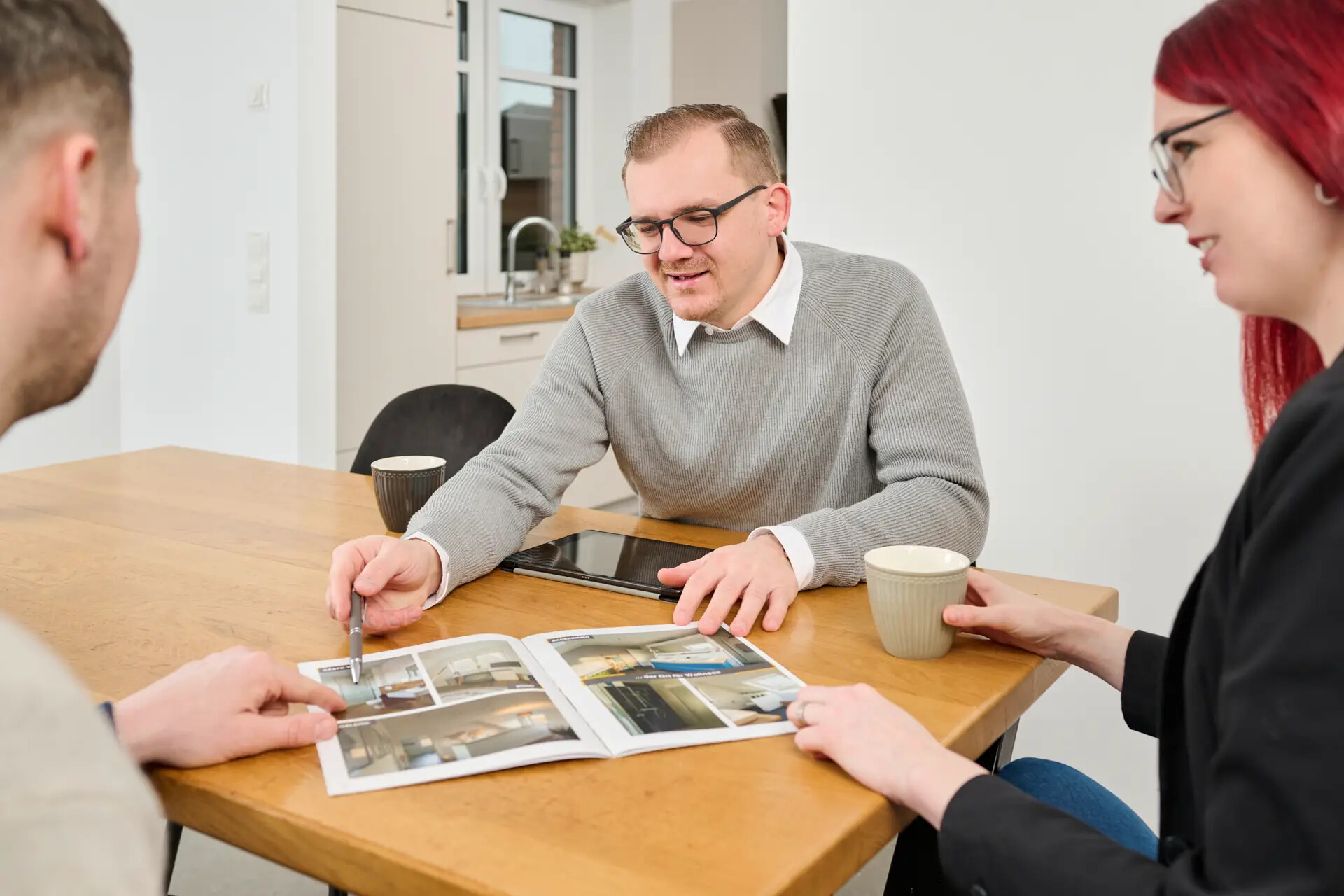 Drei Personen besprechen Fotos an einem Tisch mit Kaffee und Tablet.