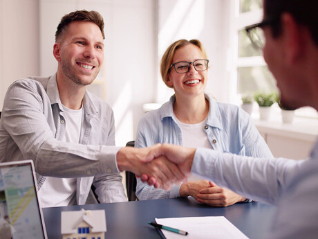 Lächelndes Paar schüttelt Hände mit Fachmann am Schreibtisch.