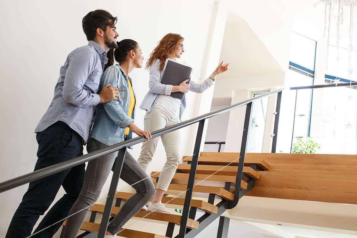 Drei Personen gehen eine Treppe hinauf, eine Frau zeigt nach vorn.