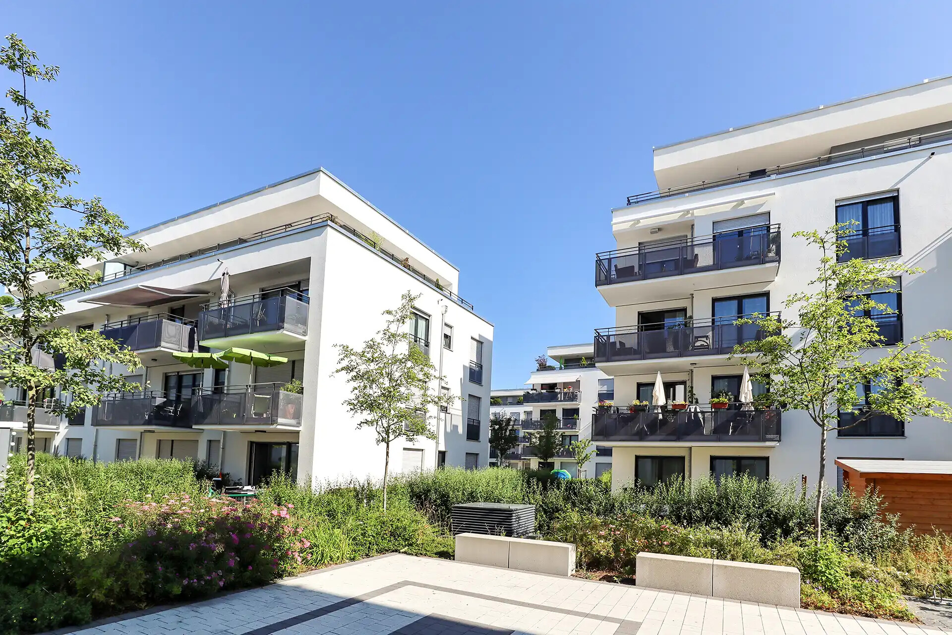 Weiße Apartmenthäuser mit Balkonen und Grün vor blauem Himmel.