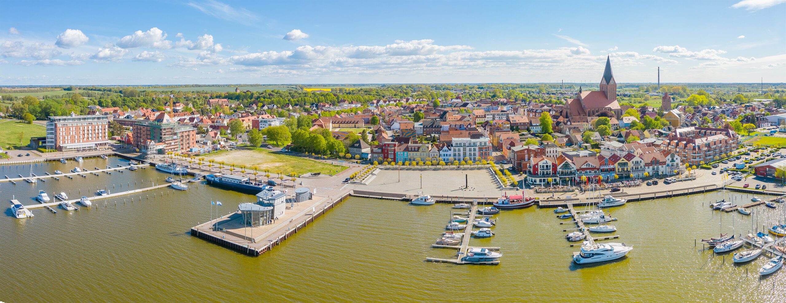 Marina mit Booten, Uferhäusern und Kirche an einem sonnigen Tag.