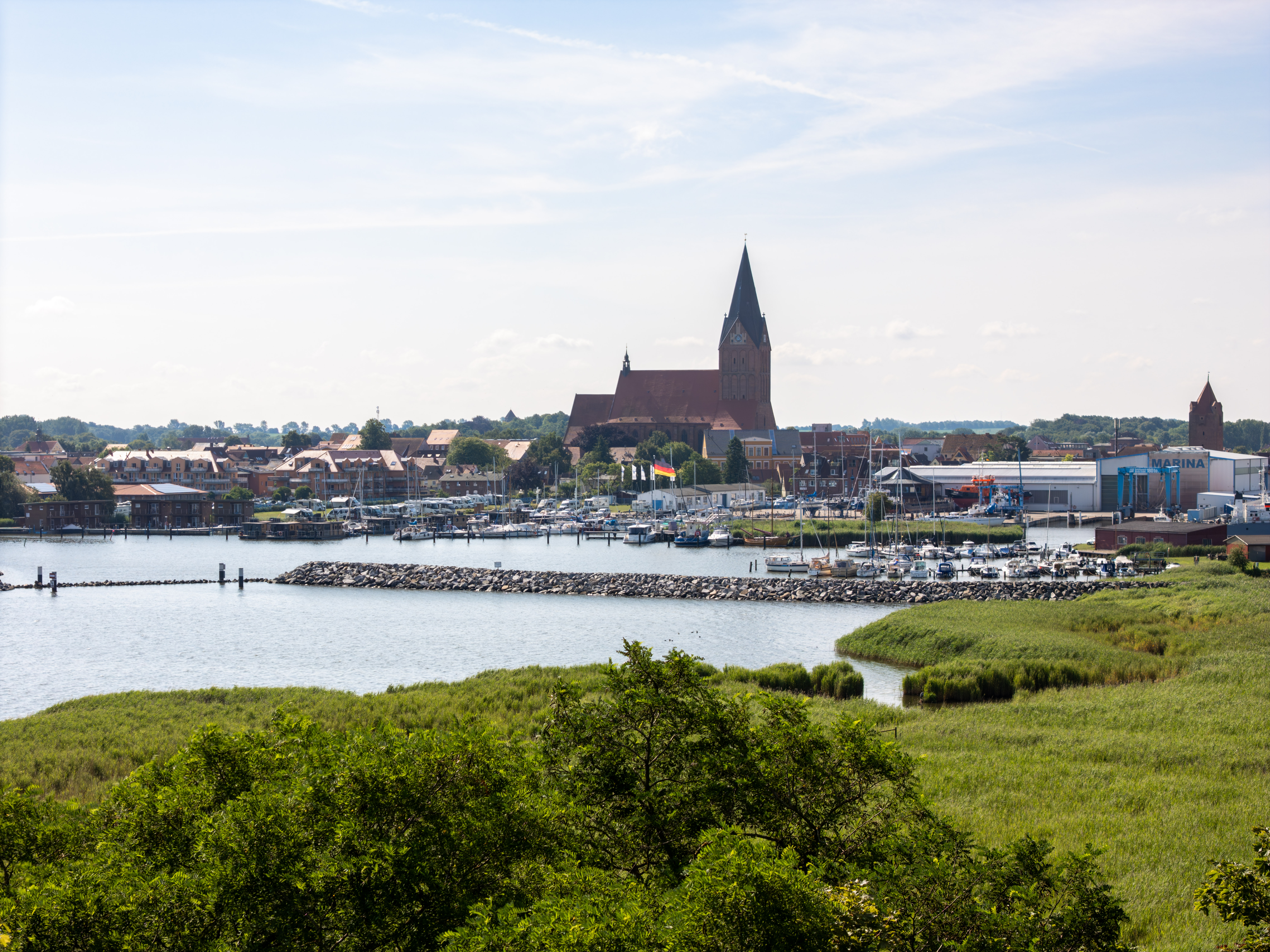 Küstenstadt mit großer Kirche, Yachthafen und grünen Feldern.