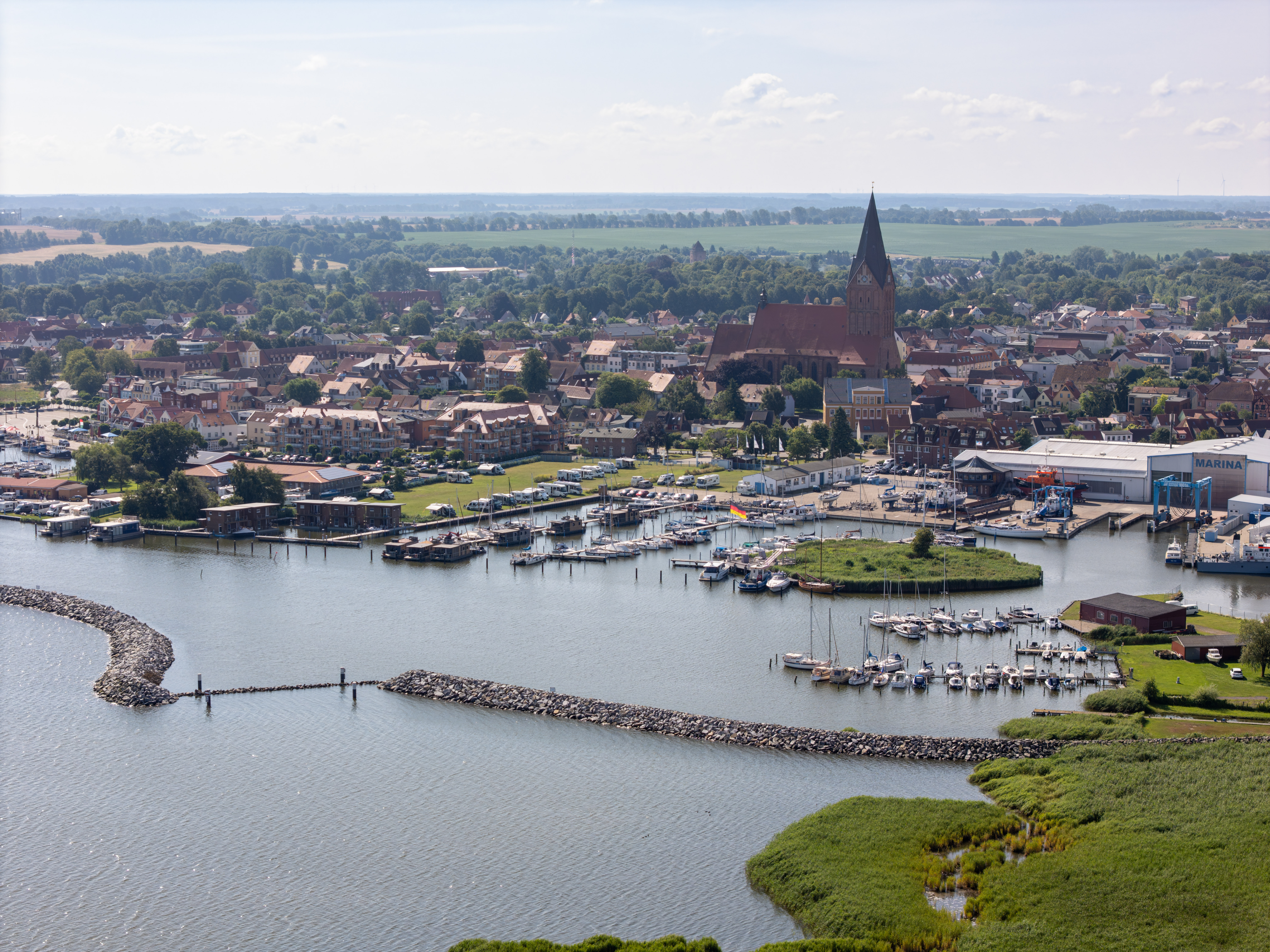 Hafen mit Booten, kleinem Ort und großer Kirche bei Sonnenschein.