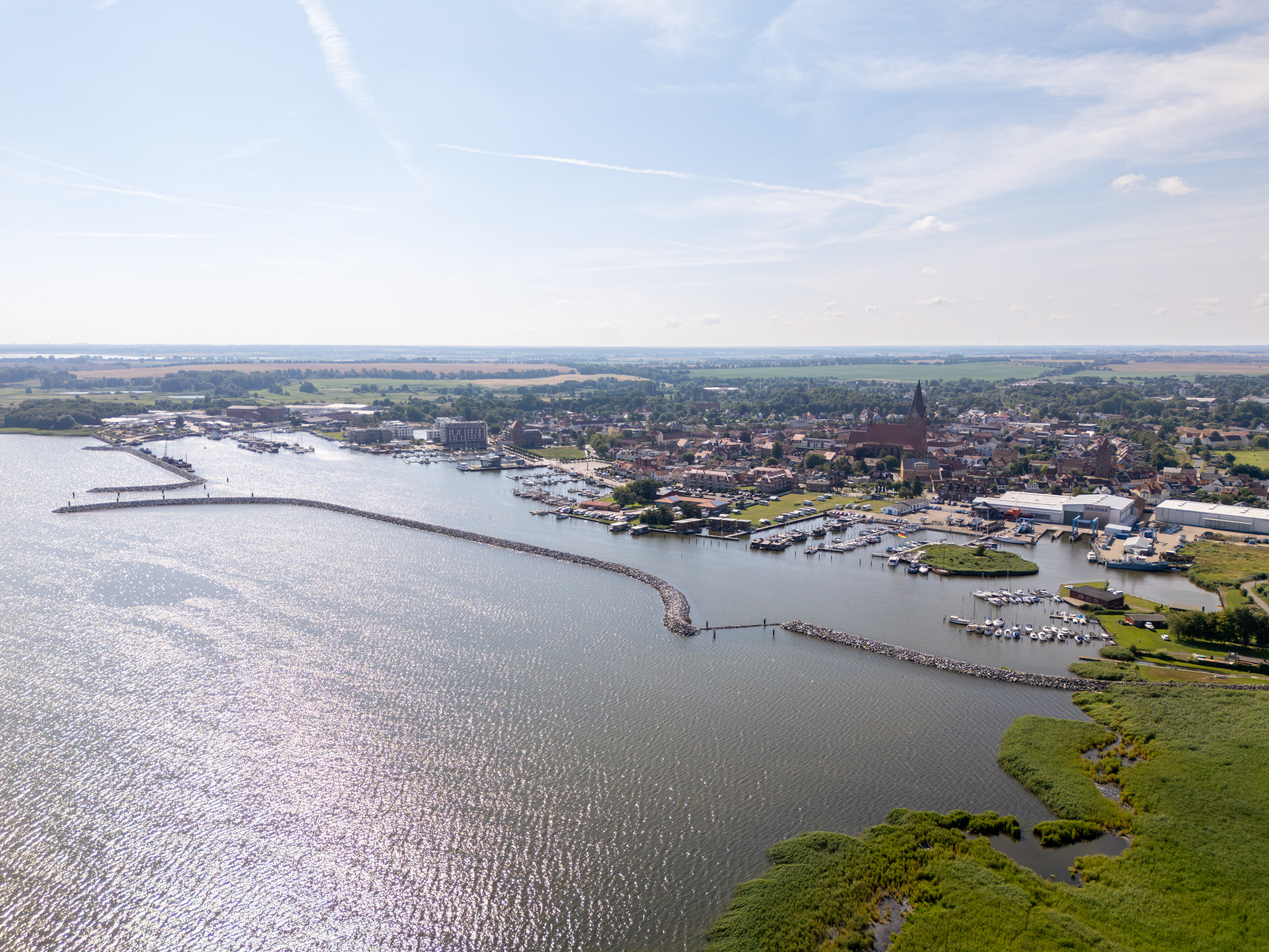 Küstenstadt mit Marina, Wellenbrecher und grüner Küste.