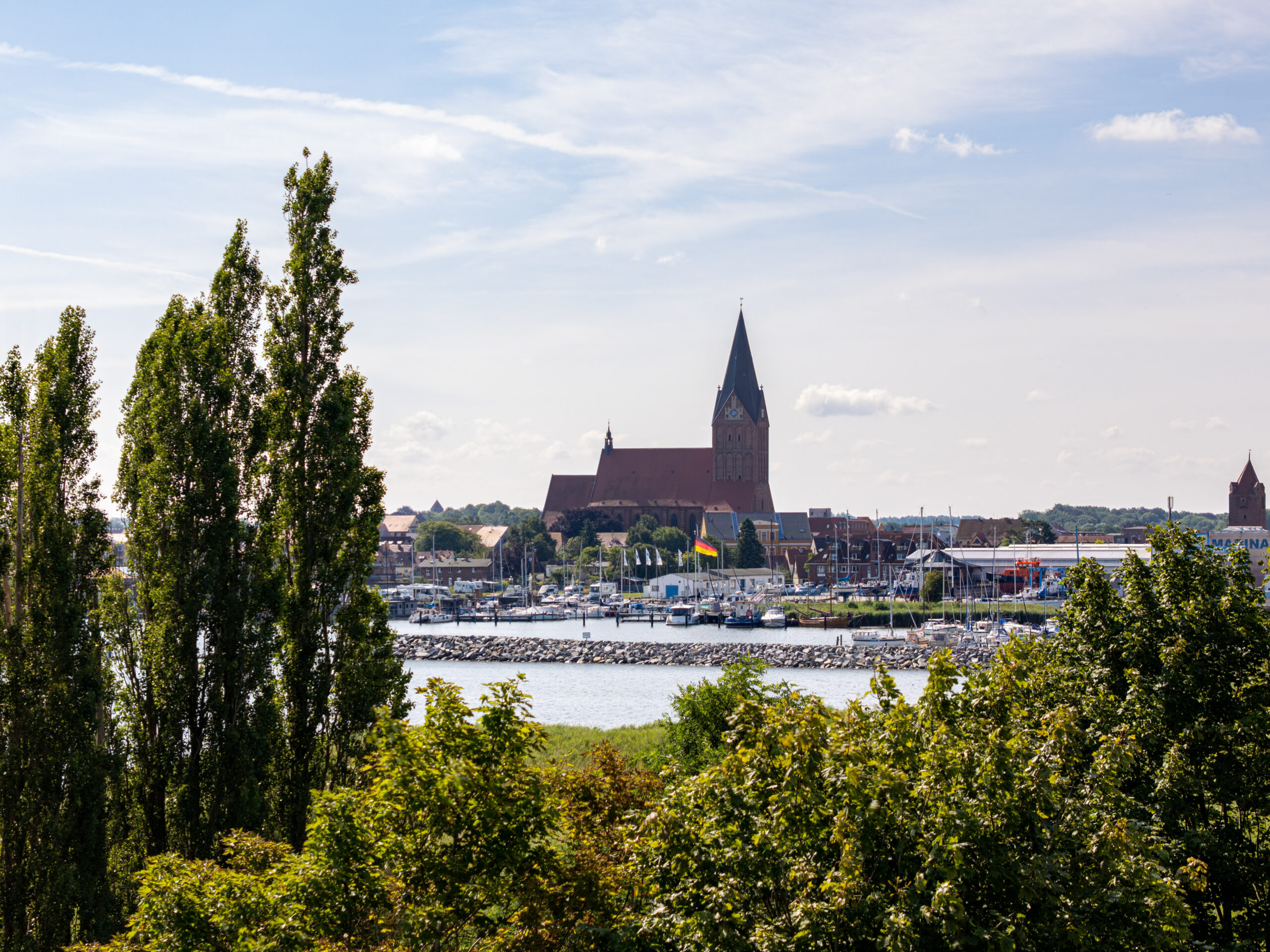 Stadt am Fluss mit Kirche, Marina und Bäumen unter blauem Himmel.
