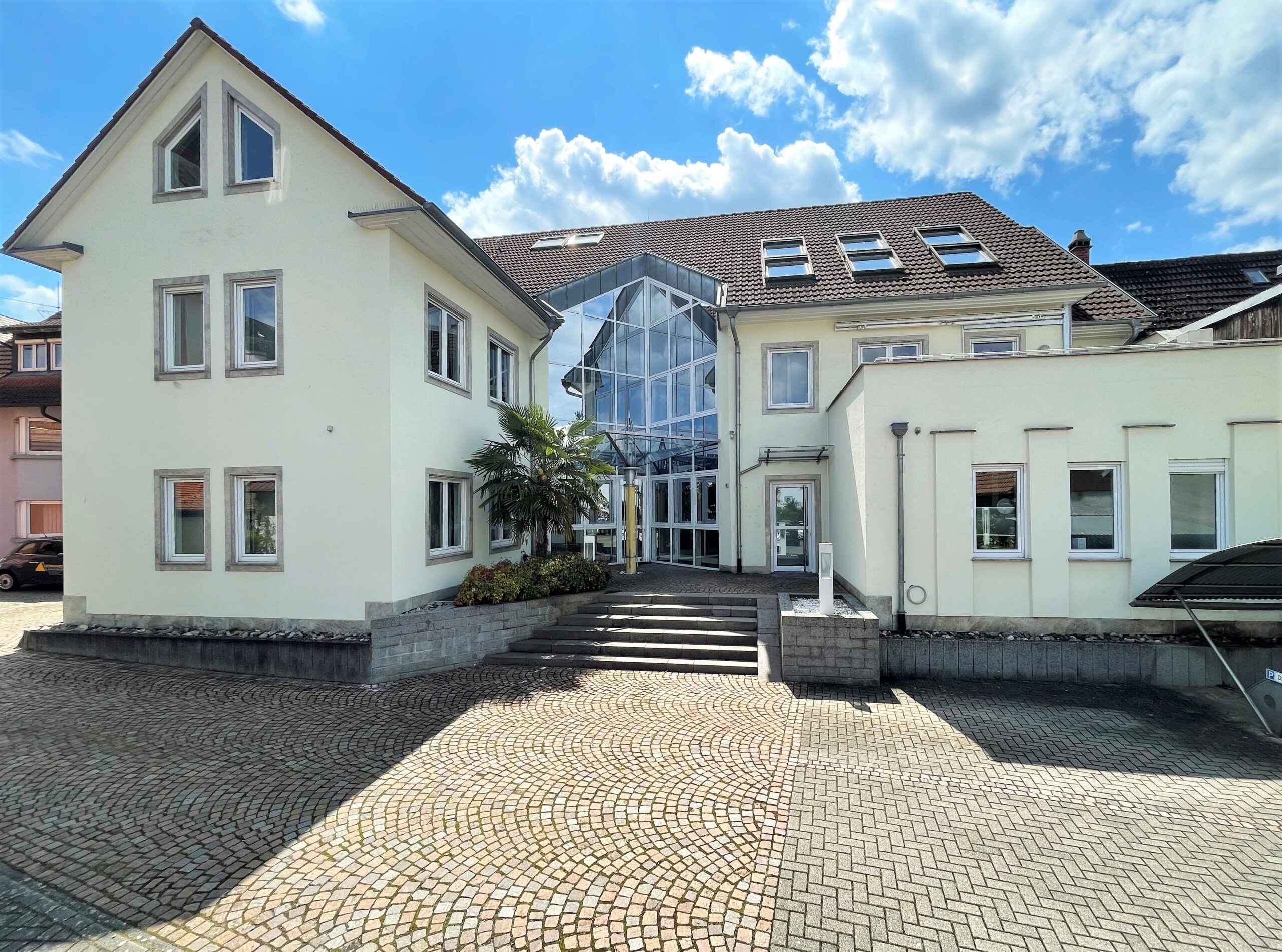 Modernes Gebäude mit Glaseingang und Innenhof unter blauem Himmel.