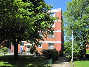 Wohnung aus rotem Backstein mit Bäumen und Menschen an einem sonnigen Tag.