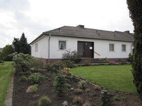 Einstöckiges weißes Haus mit braunem Dach und Gartenrasen.