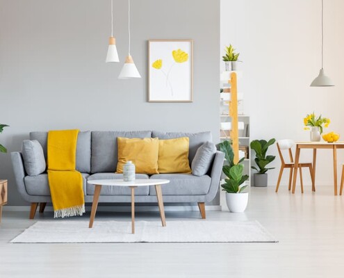 Hergerichtetes Wohnzimmer mit grauer Couch und gelben Kissen
