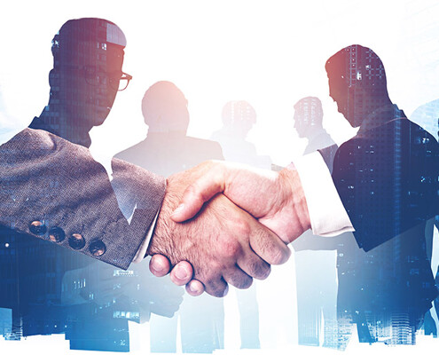 Handschlag, im Hintergrund Businessleute