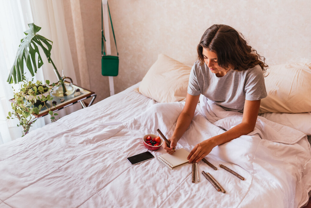 Junge Frau sitzt im Bett und macht Notizen