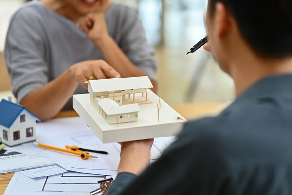 Ein Immobilienmakler zeigt einer Kundin ein Hausmodell aus Holz