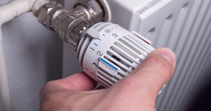 Mann dreht am Thermostat einer Heizung