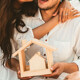 Junges glückliches Paar mit einem Modellhaus aus Holz