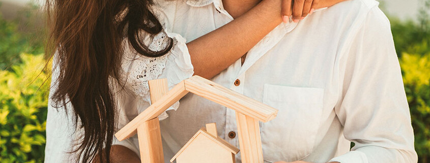 Junges glückliches Paar mit einem Modellhaus aus Holz
