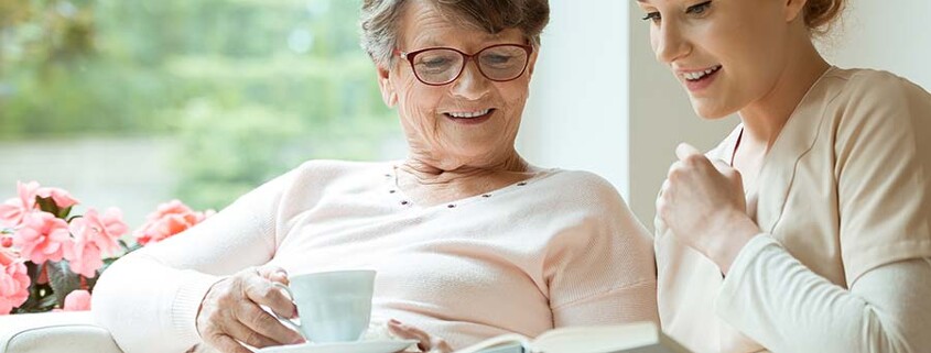 Ältere Damer hat als Wohnmöglichkeit im Alter das betreute Wohnen gewählt und schaut sich mit der Betreuerin ein Buch an