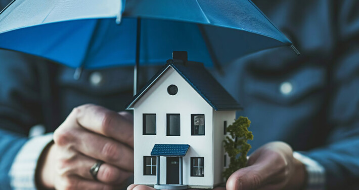 Person schützt Haus mit einem kleinen Regenschirm als Symvol für Versicherungen