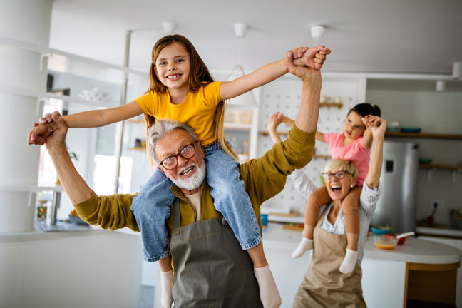 Großeltern in Haus oder Wohnung spielen mit Enkelkindern. Mit der Immobilienrente ist es möglich Nachkommen zu unterstützen, dank den Immobilienpreisen