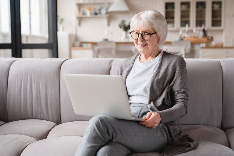 Eine Seniorin sitzt mit Laptop auf der Couch